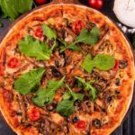 Signature Spices - A pizza with mushrooms, spinach and tomatoes on a black table
