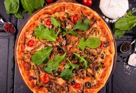 Signature Spices - A pizza with mushrooms, spinach and tomatoes on a black table