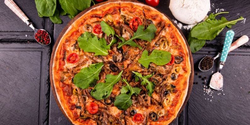 Signature Spices - A pizza with mushrooms, spinach and tomatoes on a black table