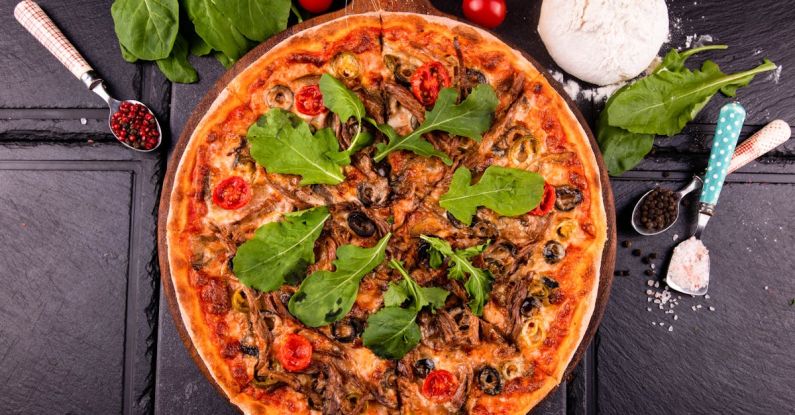Signature Spices - A pizza with mushrooms, spinach and tomatoes on a black table