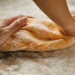 Home Chef - Unrecognizable female kneading soft fresh egg dough on cutting board with flour in kitchen