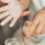 Family Recipes - Happy crop cute girl with pigtail and blurred father shaking off flour from hands while making dough