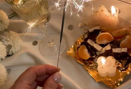 Food Festivals - From above of unrecognizable female with burning Bengal light standing near flowers wineglass and food on tray on white fabric in room with burning candles